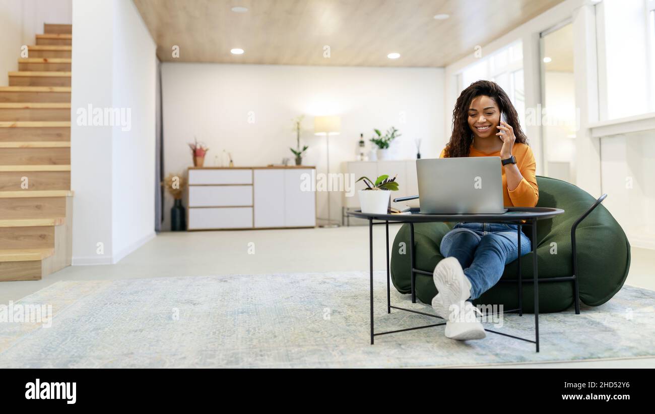 Smiling black woman working and talking on phone at home Stock Photo