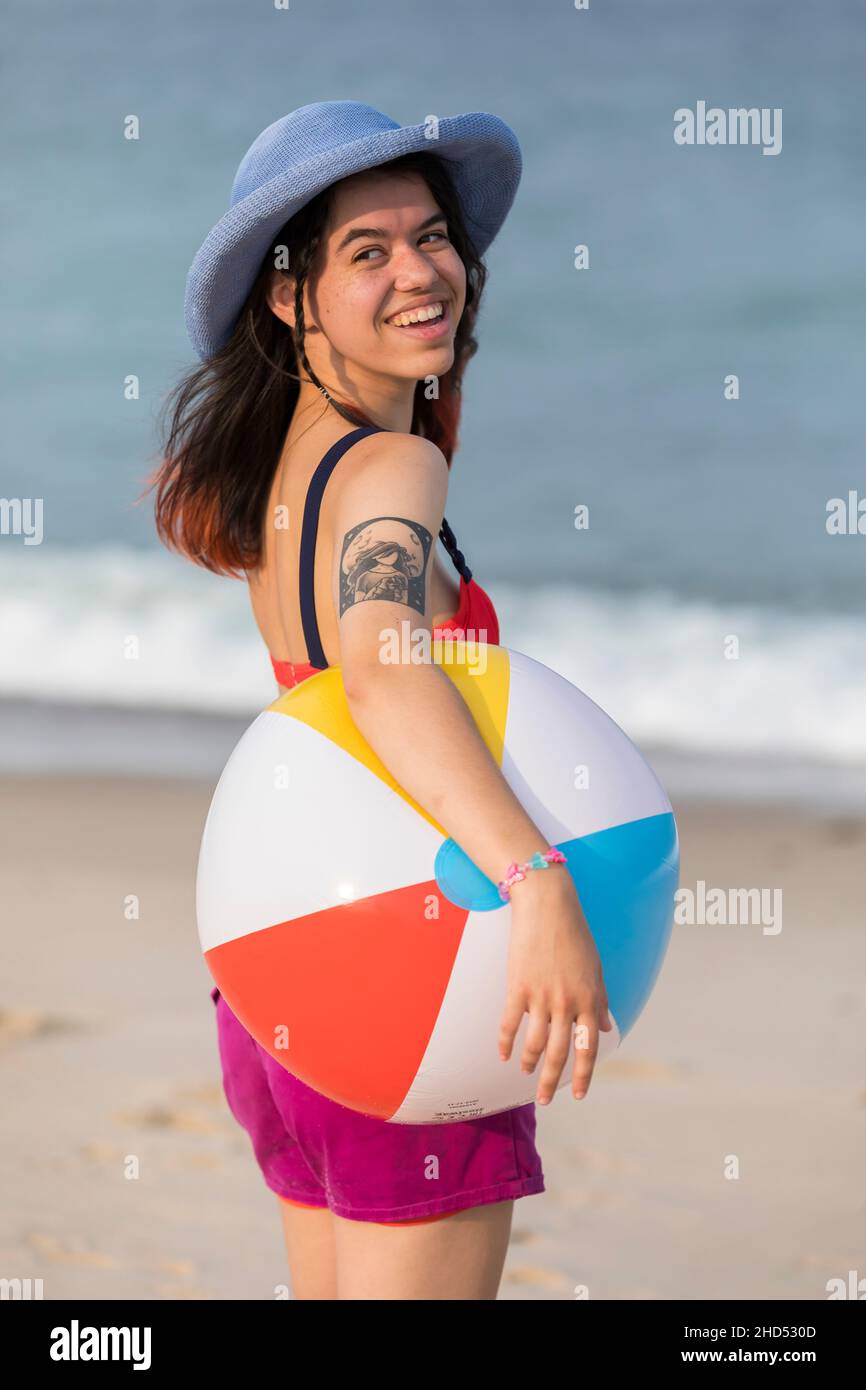 Young woman smiling at beach with beach ball and hat Stock Photo