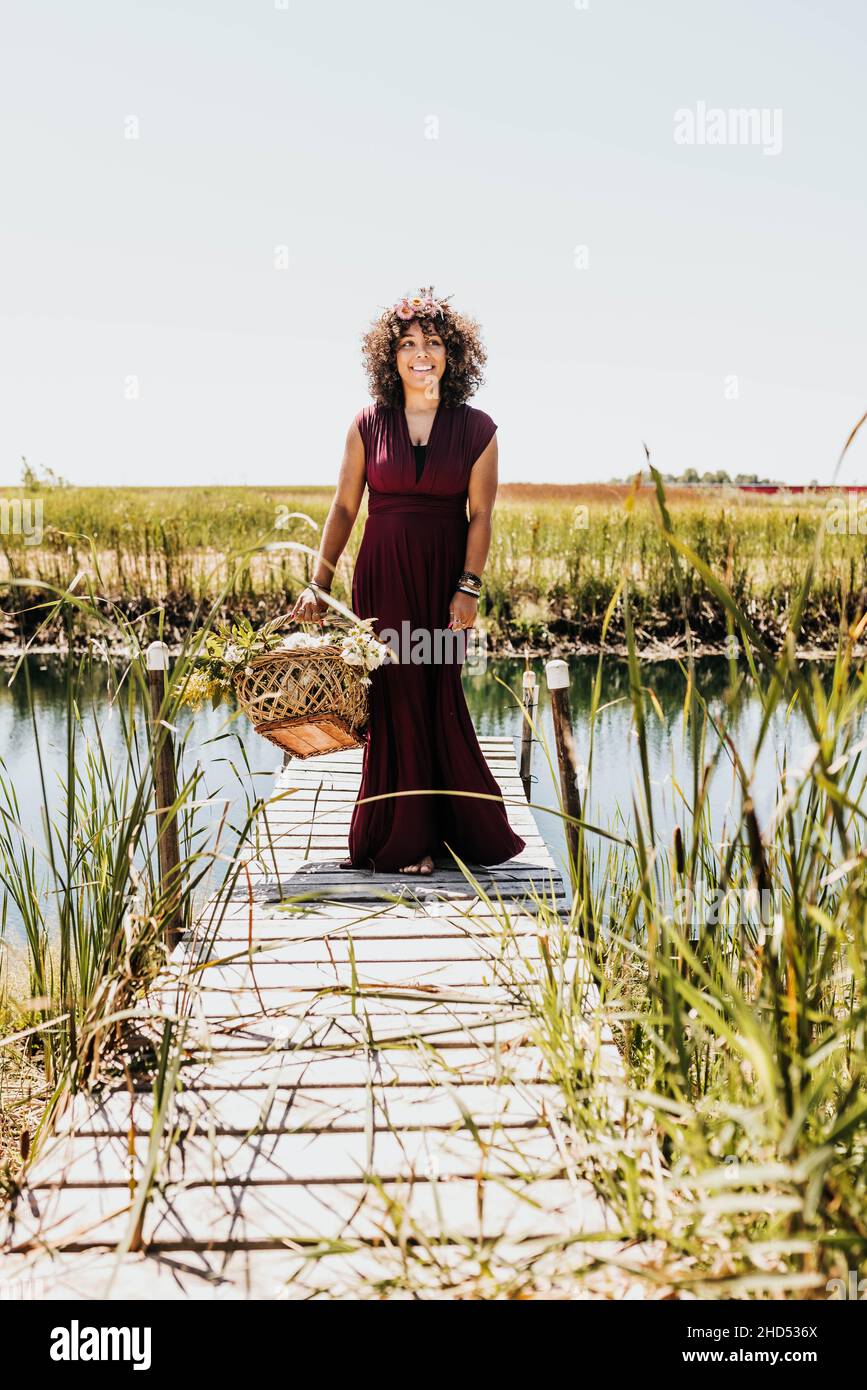 Woman walks on dock while holding woven basket full of flowers Stock Photo