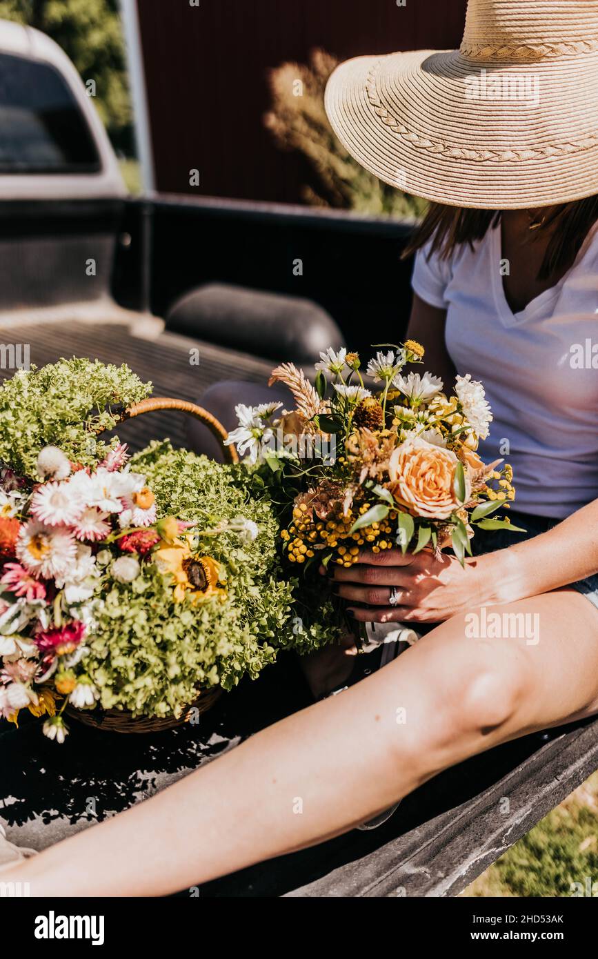 Woman sits on truck bed arranging fresh garden flowers Stock Photo