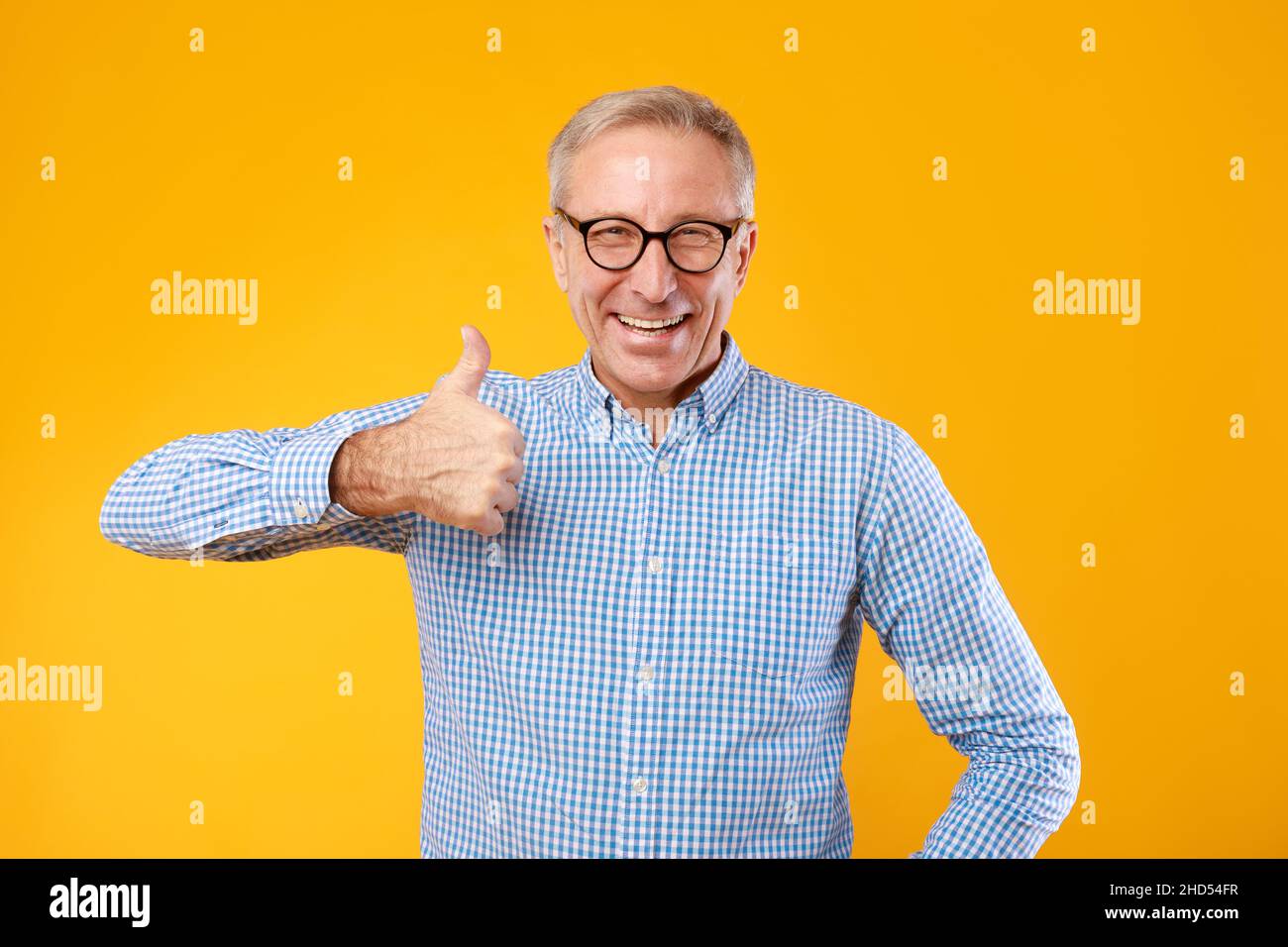 Happy mature man gesturing thumbs up and smiling at studio Stock Photo