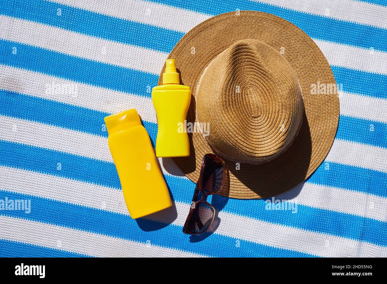 Yellow sunscreen cream bottles for skin protection, sun glasses, straw hat on the blue striped mattress. Summer recreation concept. Flat lay Stock Photo