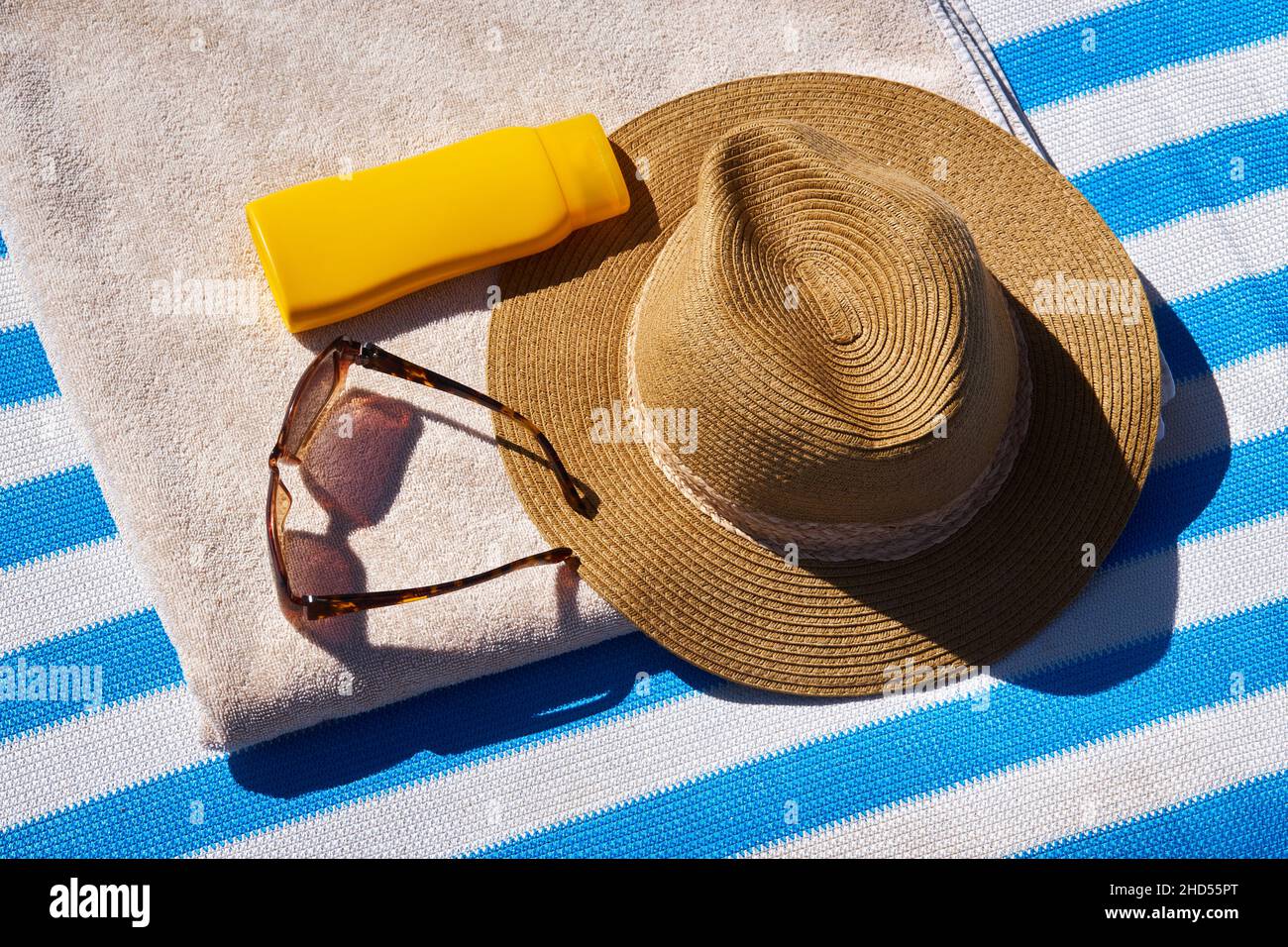 Yellow sunscreen cream bottles for skin protection, sun glasses, straw hat and beach towel on the blue striped mattress. Summer recreation concept. Fl Stock Photo