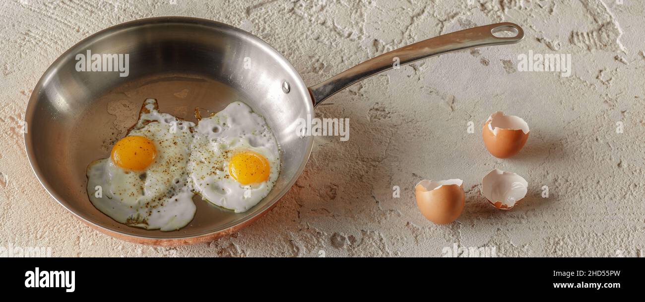 Two fried eggs in copper pan and egg shells on rough textured clay background. Healthy breakfast