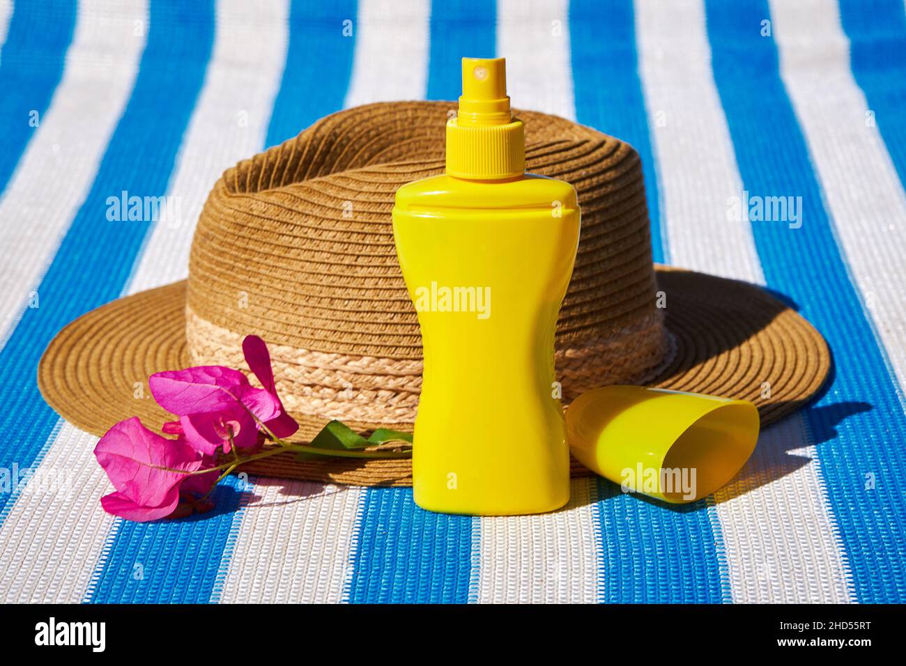 Yellow sunscreen cream bottle for skin protection, sun glasses, straw hat and beach towel on the blue striped mattress. Summer recreation concept Stock Photo