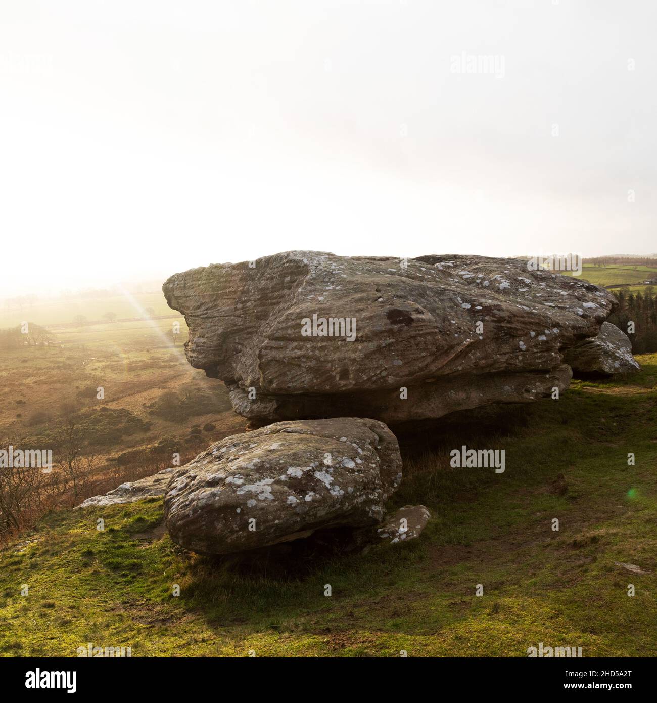 Rock overlooking countryside at Shaftoe Crags in Northumberland, England. The low winter sun gives the sky a golden hue. Stock Photo