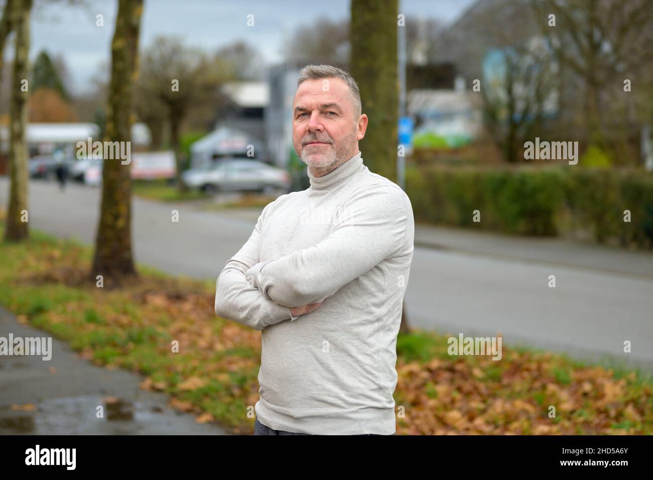 Serious confident middle-aged man with contemplative expression standing in a quiet city street looking quietly at the camera with folded arms in autu Stock Photo
