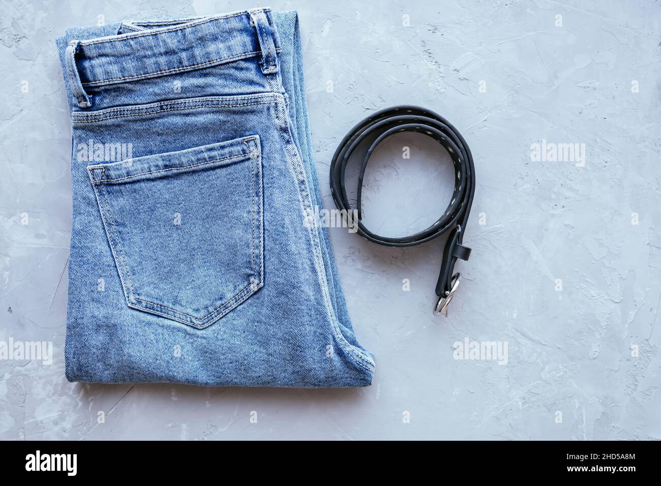 Classic blue woman jeans with belt on grey concrete background. Denim fabric. Casual wear. Top view. Comfortable style cloth. Flat lay Stock Photo