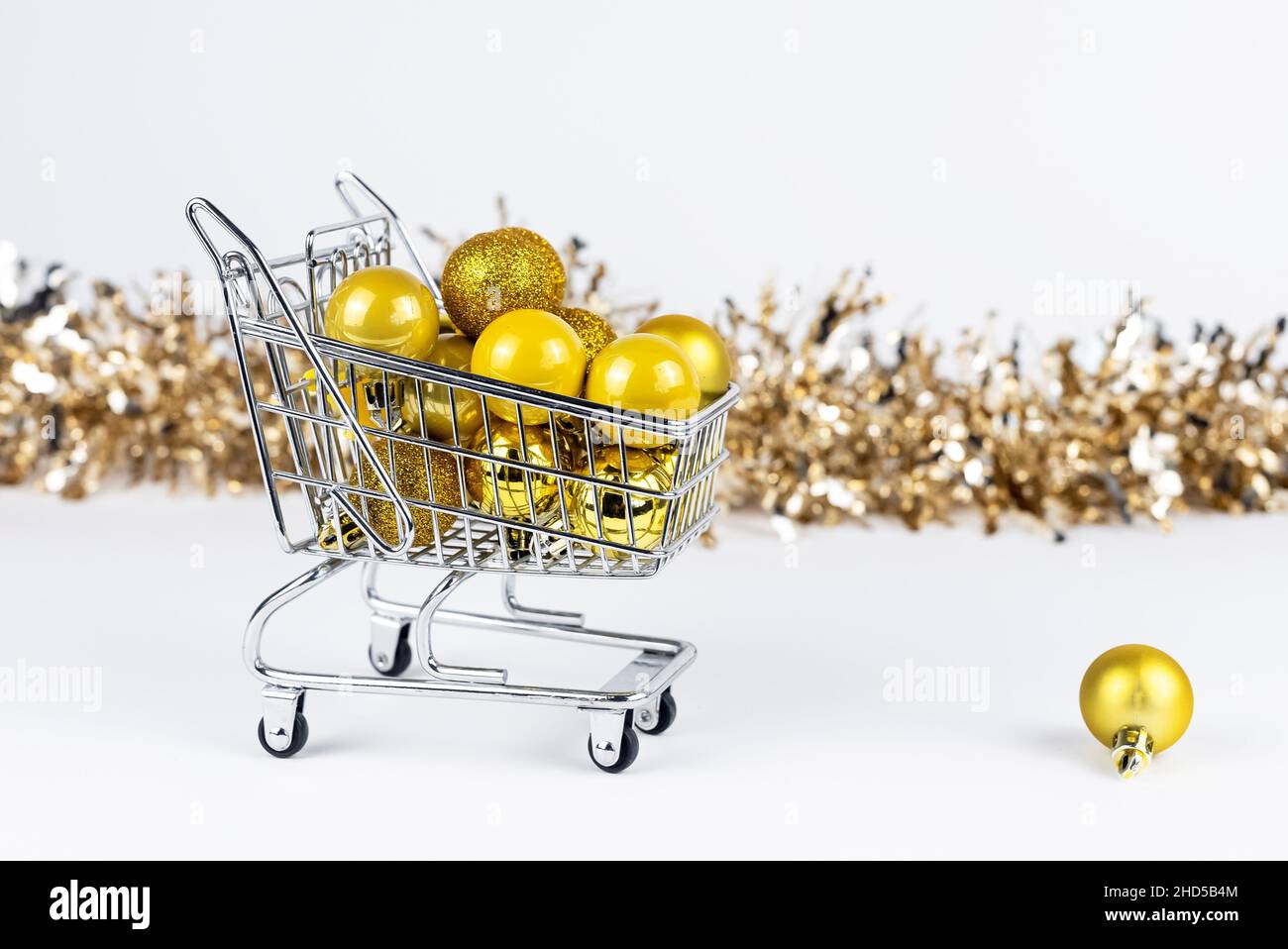 Shopping cart full of Christmas baubles, fallen ball near trolley. New Year consumerism concept. Stock Photo