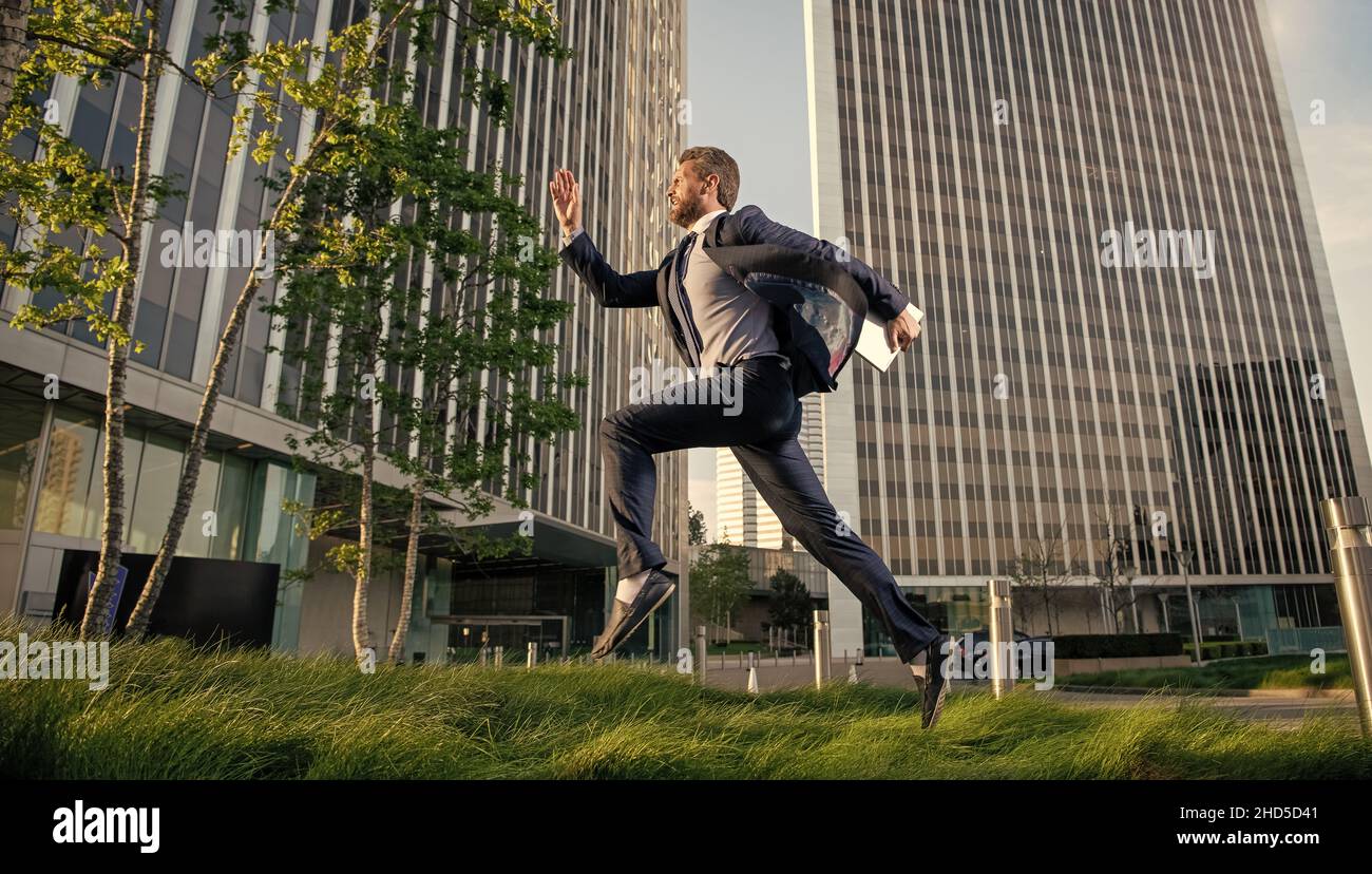 successful man in formalwear running with computer outside the office, hurry up Stock Photo