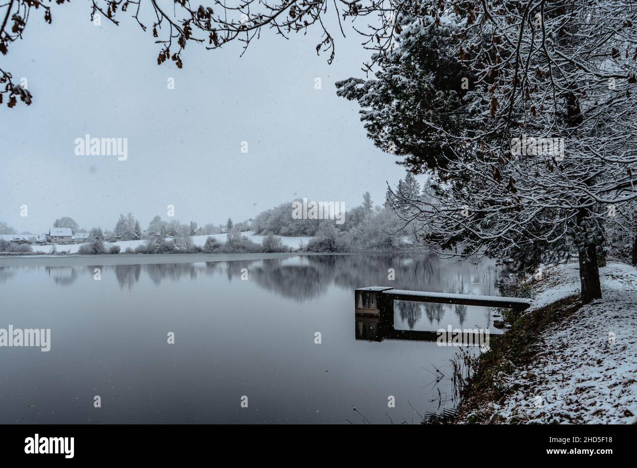 Wooden pier on lake with fresh snow.Winter pond with small jetty on misty morning.Foggy cloudy landscape reflected in water. White winter countryside Stock Photo