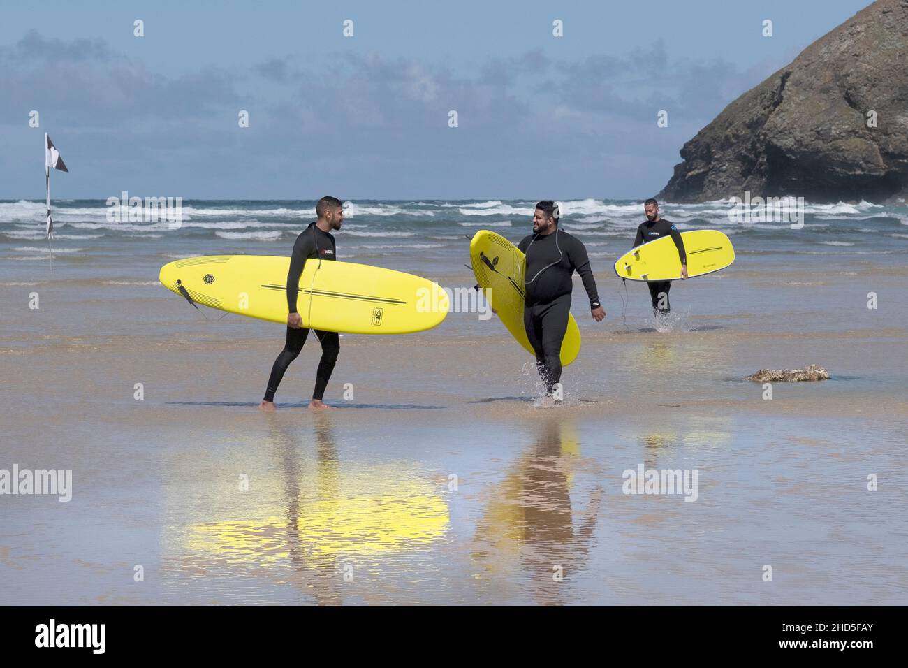 A group of male holidaymakers carrying bright yellow hired surfboards at Mawgan Porth Beach in Cornwall. Stock Photo
