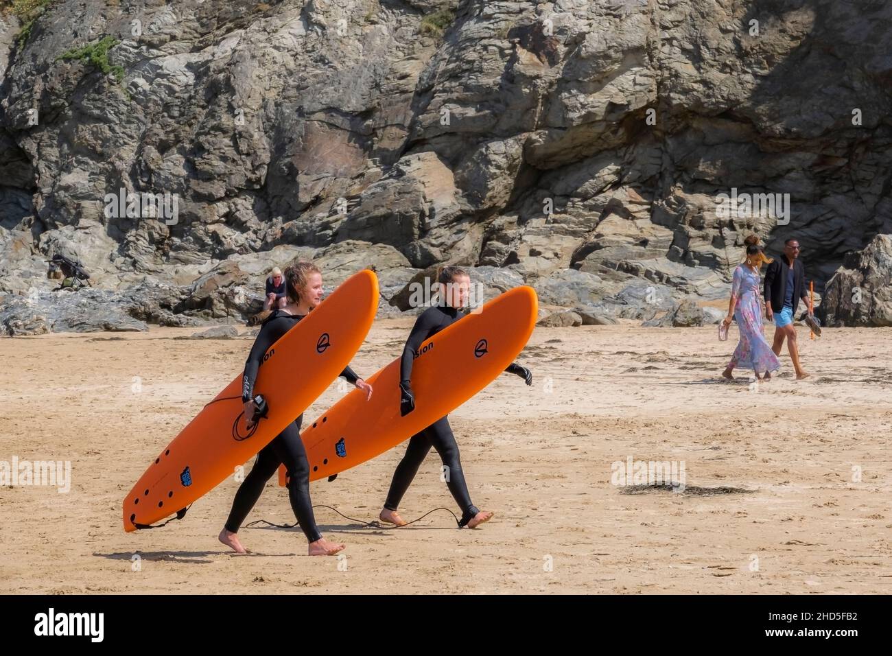 Two female holidaymakers carrying their hired colourful surfboards walking across Mawgan Porth Beach in Cornwall. Stock Photo