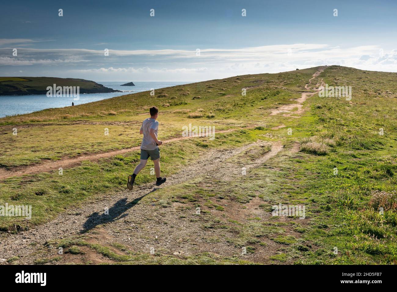 A man running along a track on The Warren leading up to the remains of the Bronze Age barrow on Pentire Point East in Newquay in Cornwall. Stock Photo