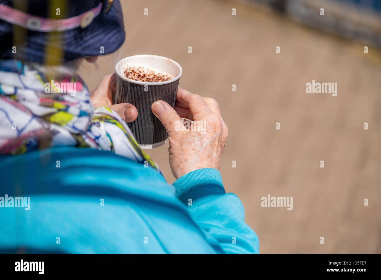 A mature person holding a cappuccino coffee in a disposable cup. Stock Photo