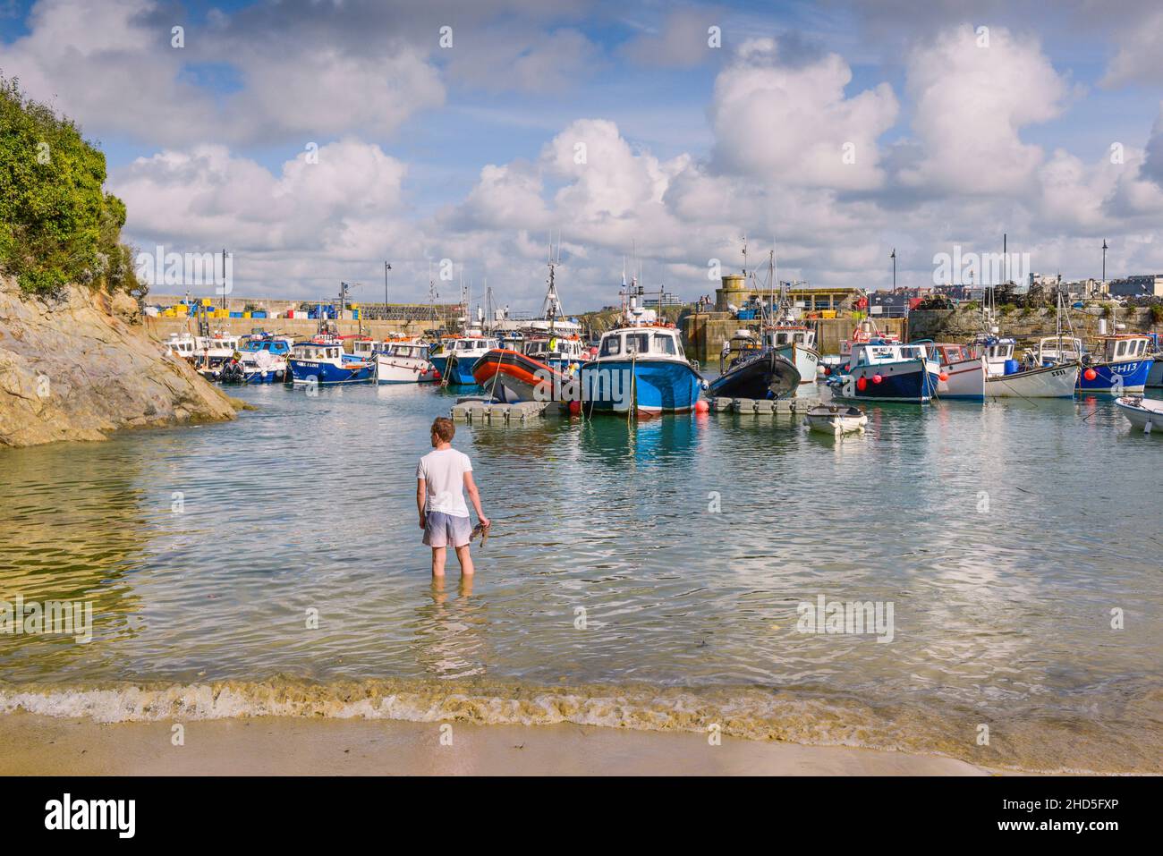 A man standing in the sea at the historic working Newquay Harbour in Newquay in Cornwall. Stock Photo