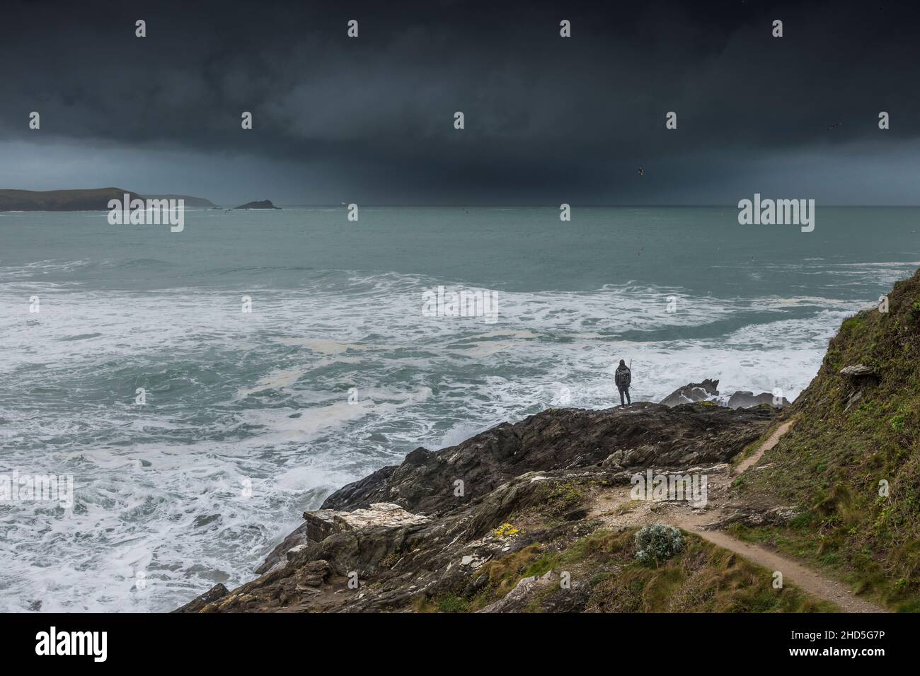 An angler standing on rocks watching dramatic storm clouds approaching Fistral Bay in Newquay in Cornwall. Stock Photo