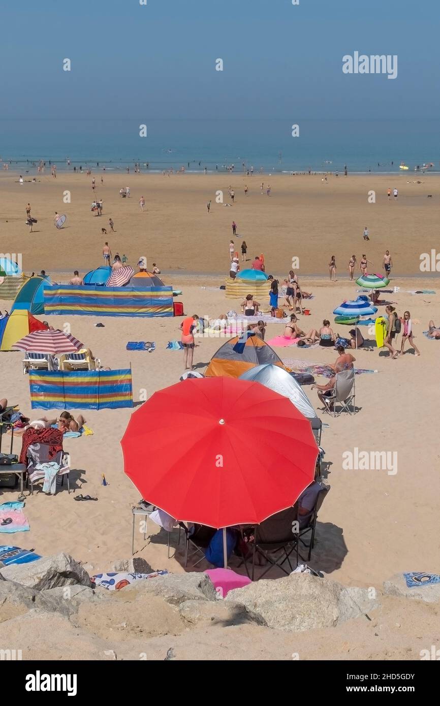 A vibrant red parasol used by holidaymakers on a busy Fistral Beach in the summer holidays in Newquay in Cornwall. Stock Photo