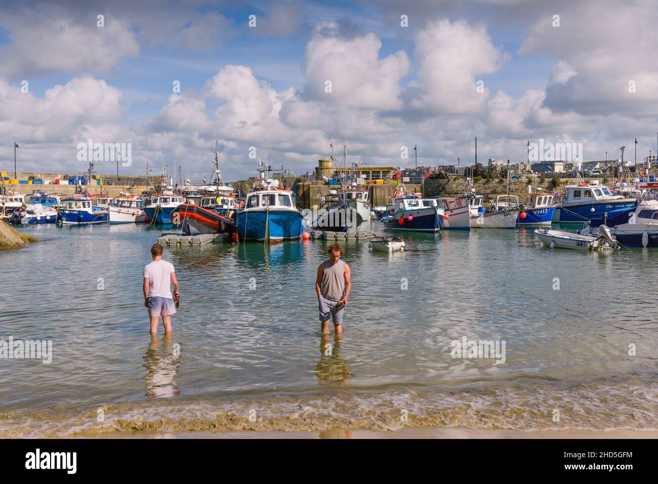 Two men standing in the sea in the historic picturesque working Newquay Harbour in Newquay in Cornwall. Stock Photo