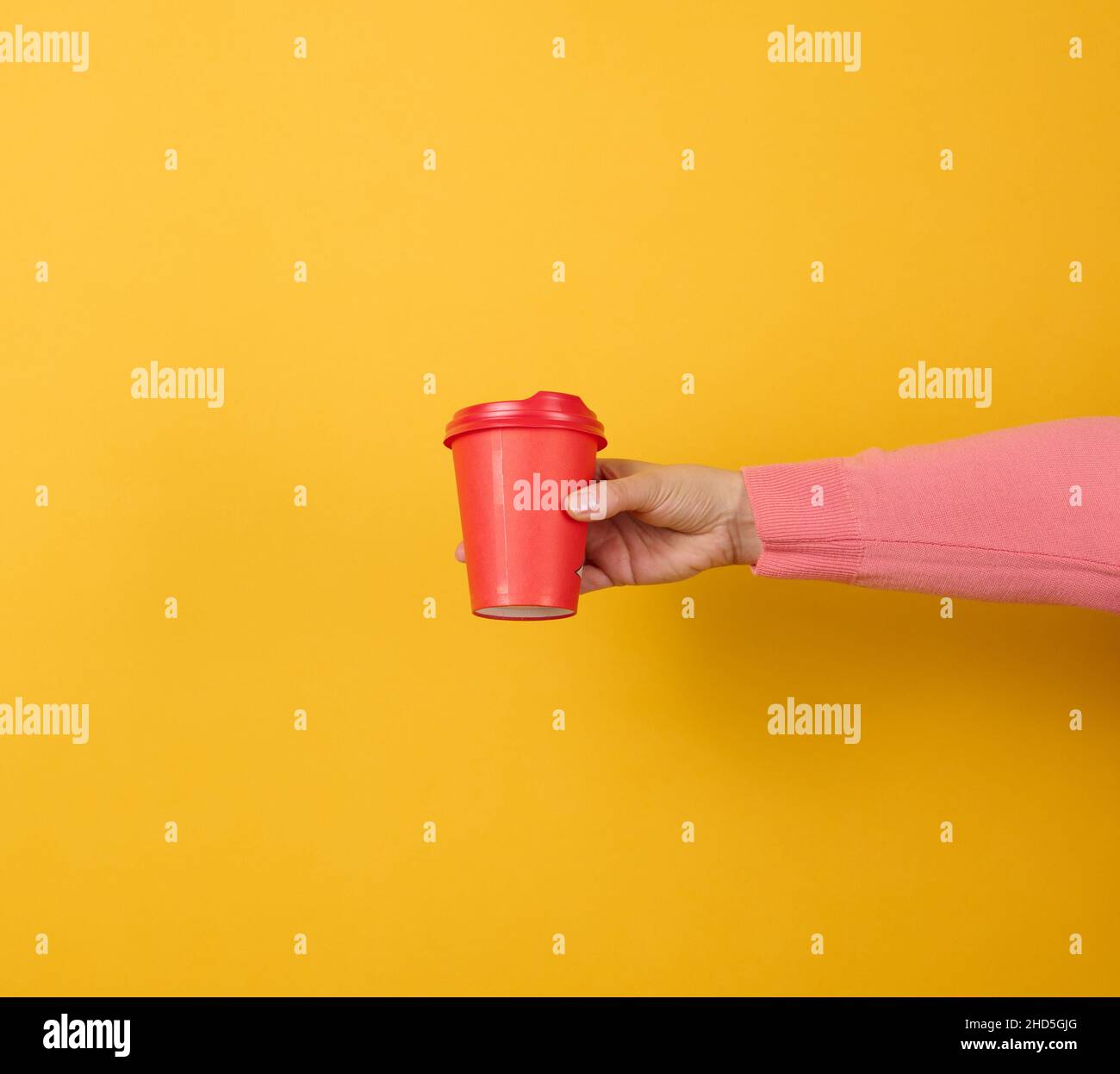 hand holds paper cardboard red cup for coffee, yellow background. Eco ...
