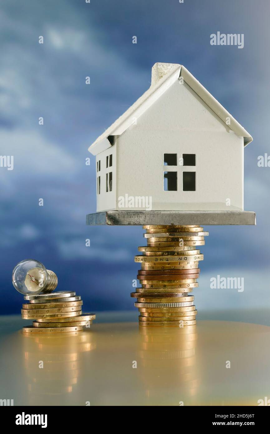 miniature metal house standing on a high stack of golden coins and a small light bulb, creative concept Stock Photo