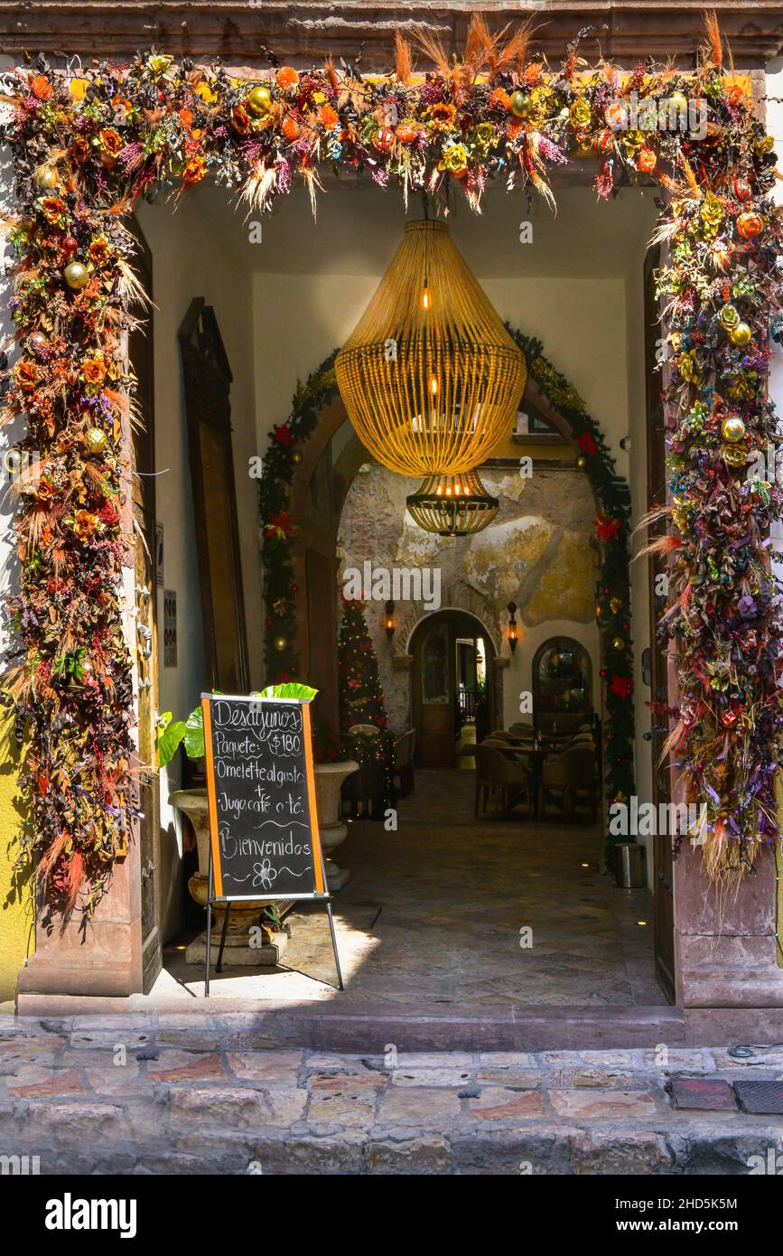 A charmingly decorative entryway made from flowers surrounding the door-frame to the reception and restaurant with sign in San Miguel de Allende, MX Stock Photo