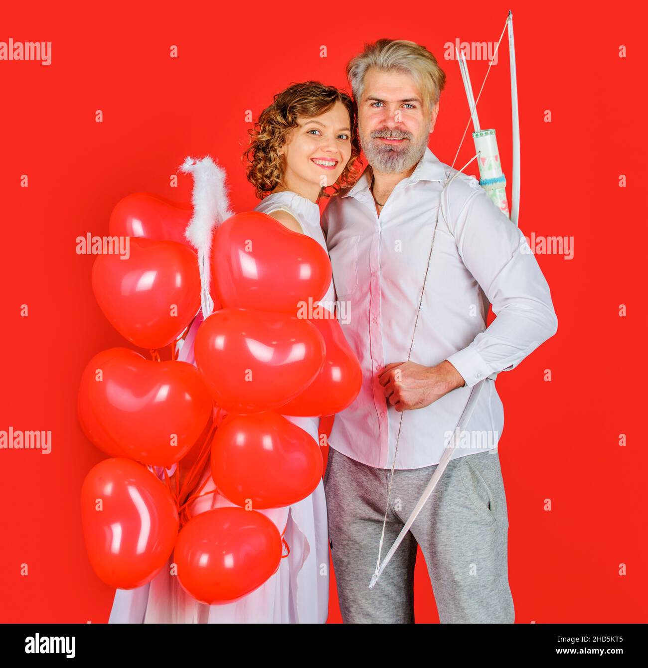 Valentines Day couple. Smiling Angel girl with balloons, happy bearded man with bow and arrows Stock Photo