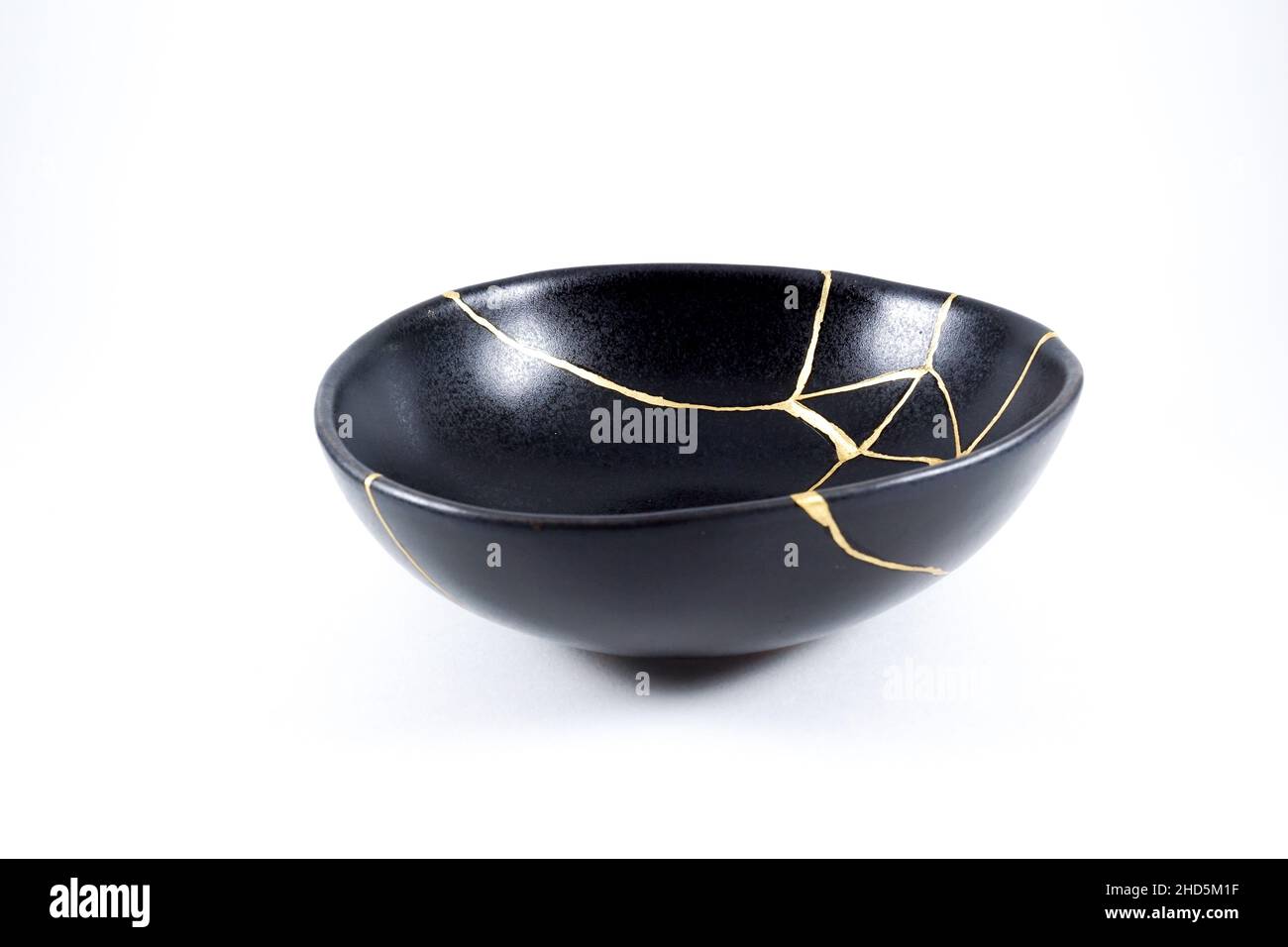 kintsugi gold cracks restoration, Japanese black bowl fixed with the antique kintsukuroi restoration technique, the beauty of imperfections, represent Stock Photo