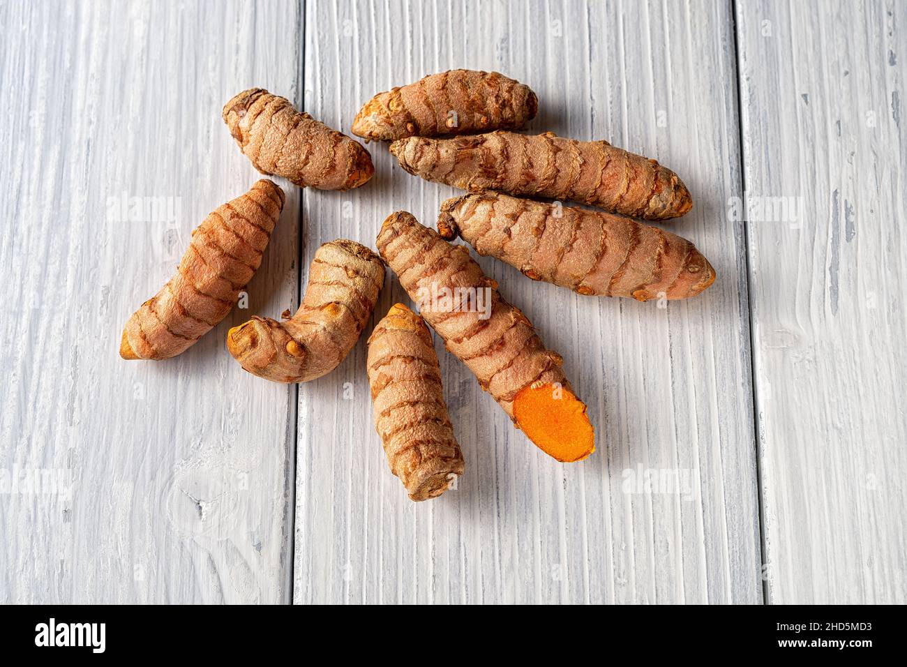 Fresh whole turmeric roots on a white wooden table. Raw organic curcuma rhizomes close-up. Curcuma longa is spice, curry powder ingredient. Stock Photo