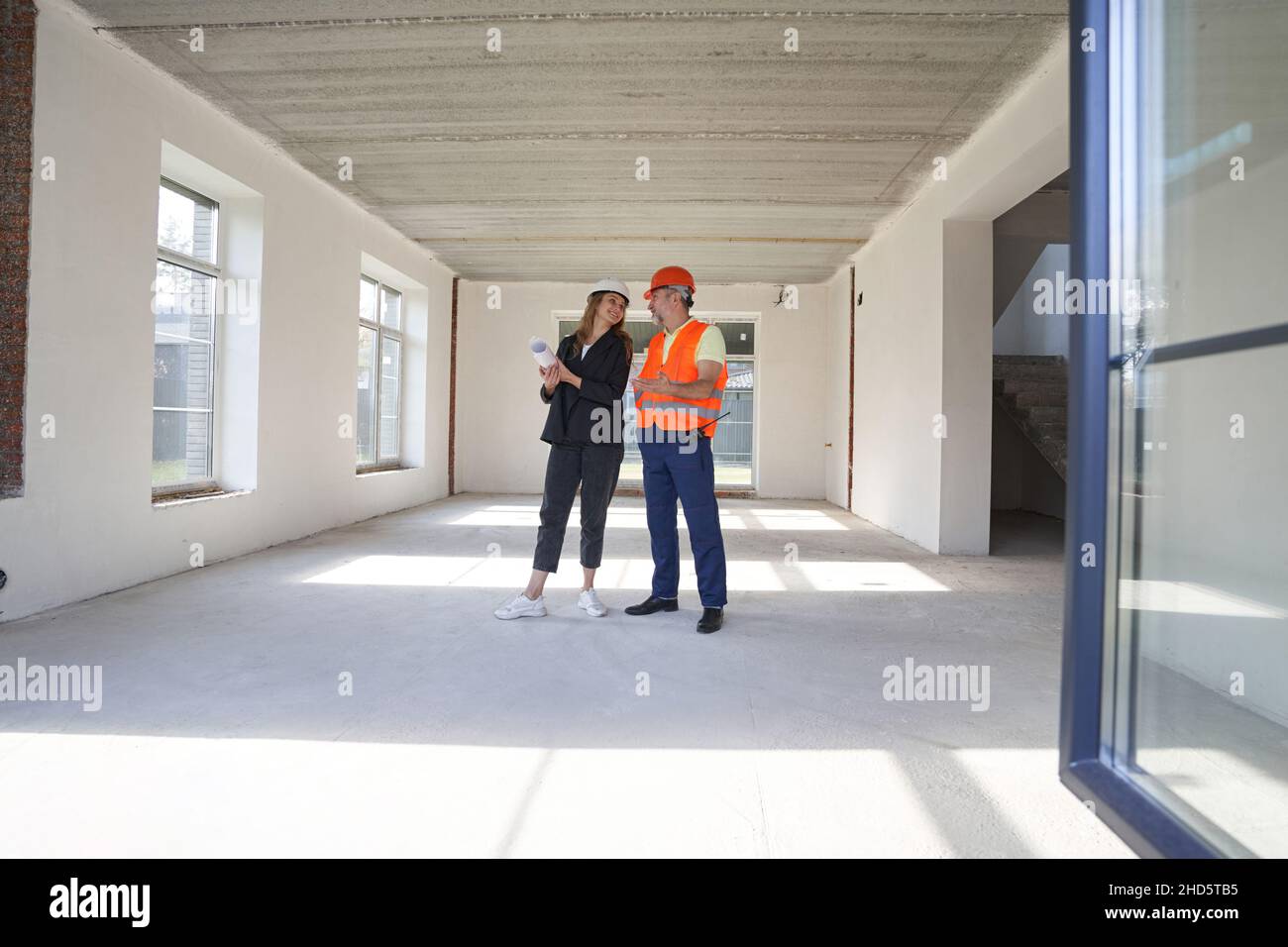 Woman engineer talking with construction worker inside house Stock Photo