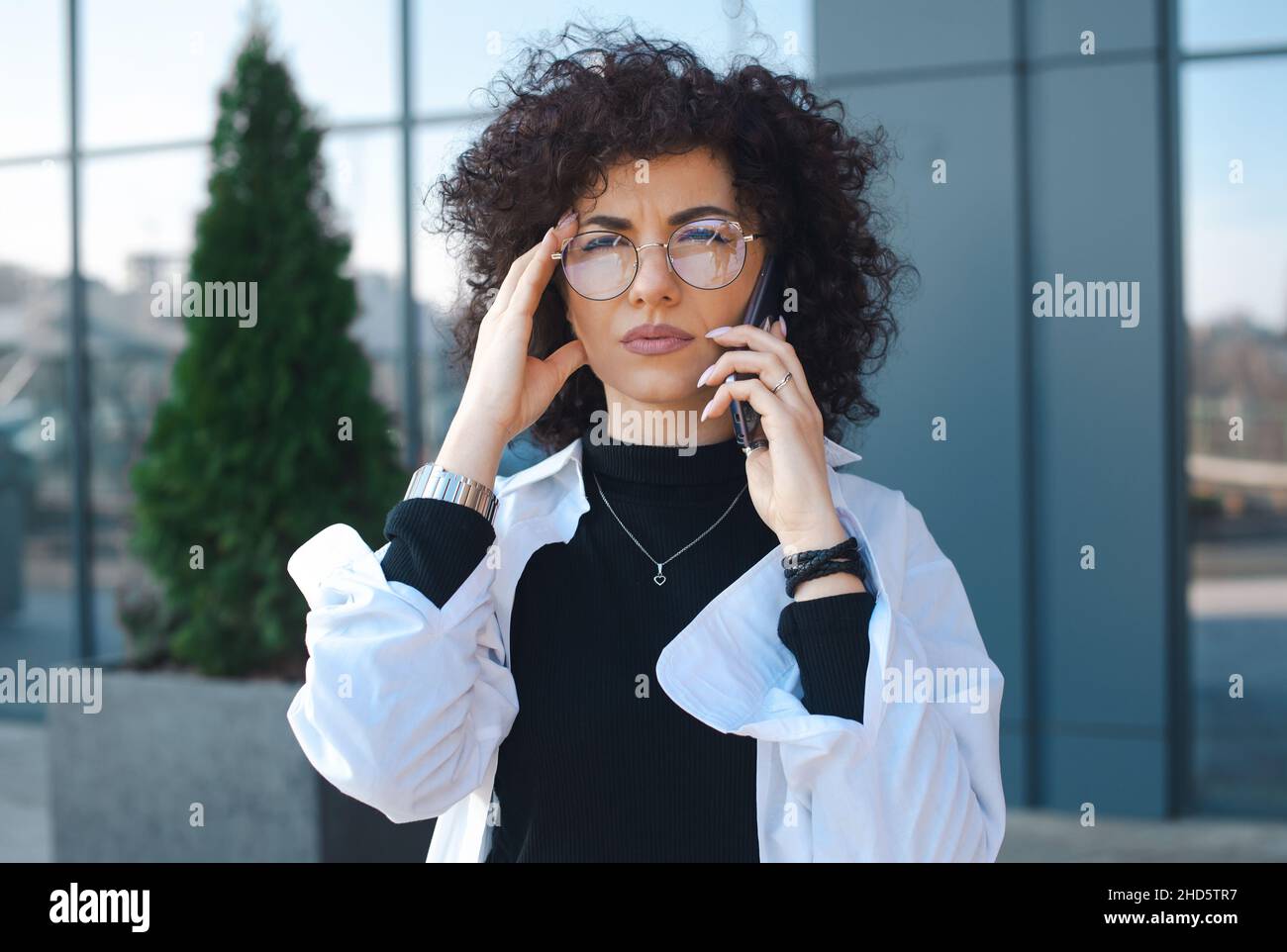 Curly manager frowning concerned speaking on cellphone outside. Close-up portrait of a caucasian woman looking on camera. Mobile phone talk concept Stock Photo