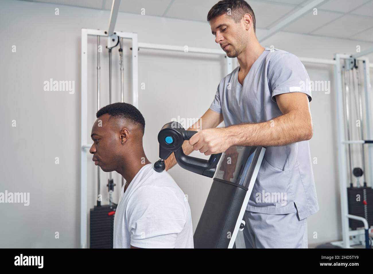 Concentrated physical therapist performing percussive therapy session Stock Photo