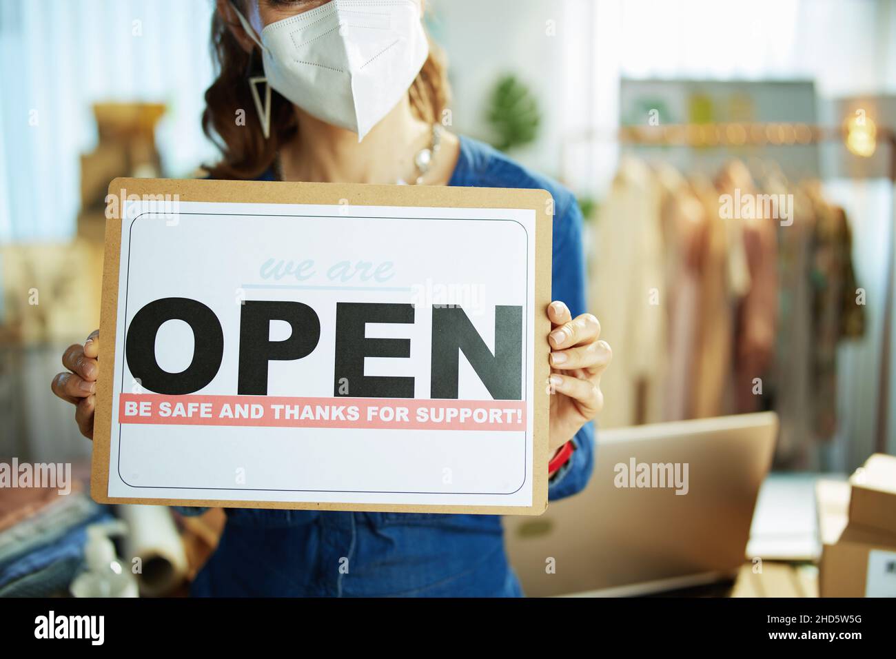 Closeup on small business owner woman with ffp2 mask and open after covid sign in the office. Stock Photo