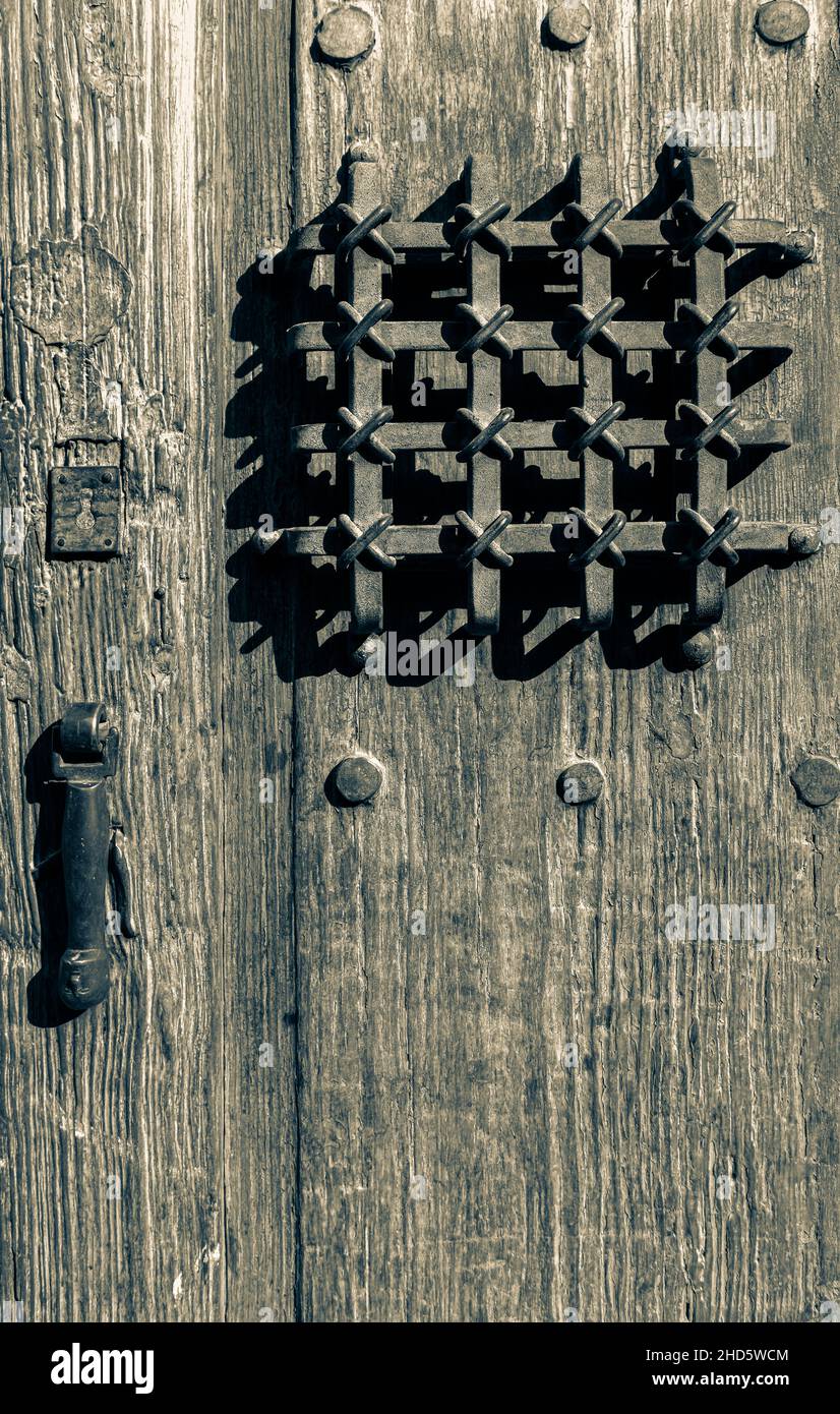 A cross-stitch pattern of ornamental metal art along with handle in stylized human form in metal on rustic, antique wooden door in Mexico in split ton Stock Photo