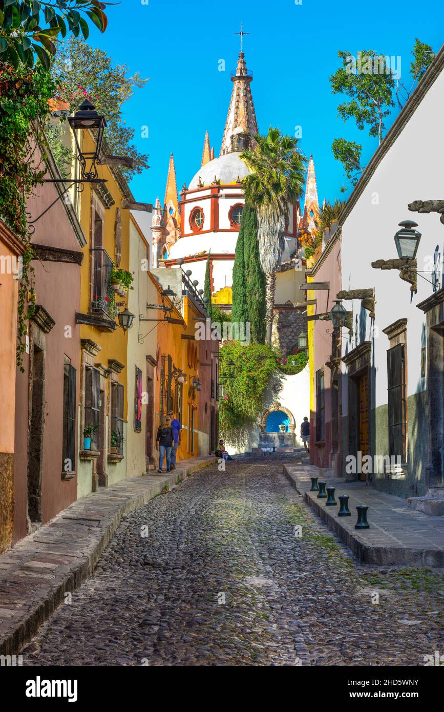 Narrow Cobblestone Aldama street offers View of the Parroquia San Miguel de Allende Archangel Church Dome  alongside homes and sidewalks in San Miguel Stock Photo
