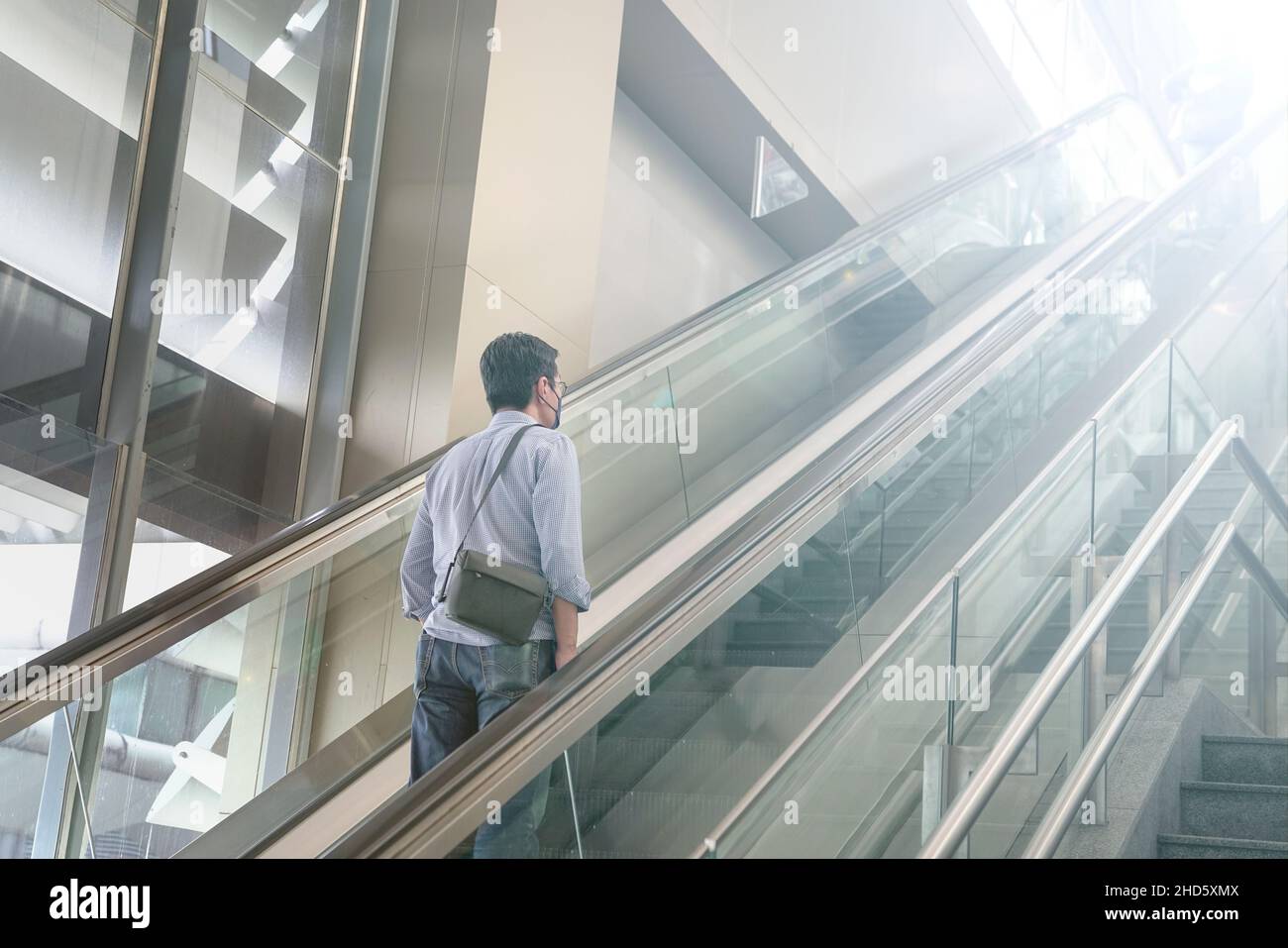 Asian man traveler with face mask on escalator inside a modern building Stock Photo