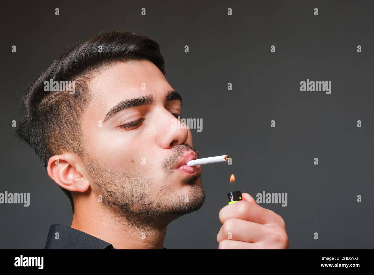 Young handsome unshaven guy lighting up cigarette Stock Photo