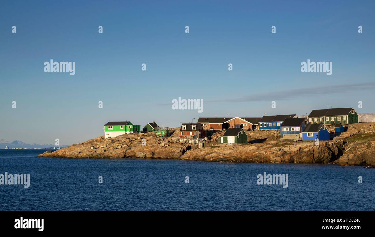 Colourful houses in Ittoqqortoormiit, with distant icebergs in Scoresby Sund, East Greenland Stock Photo