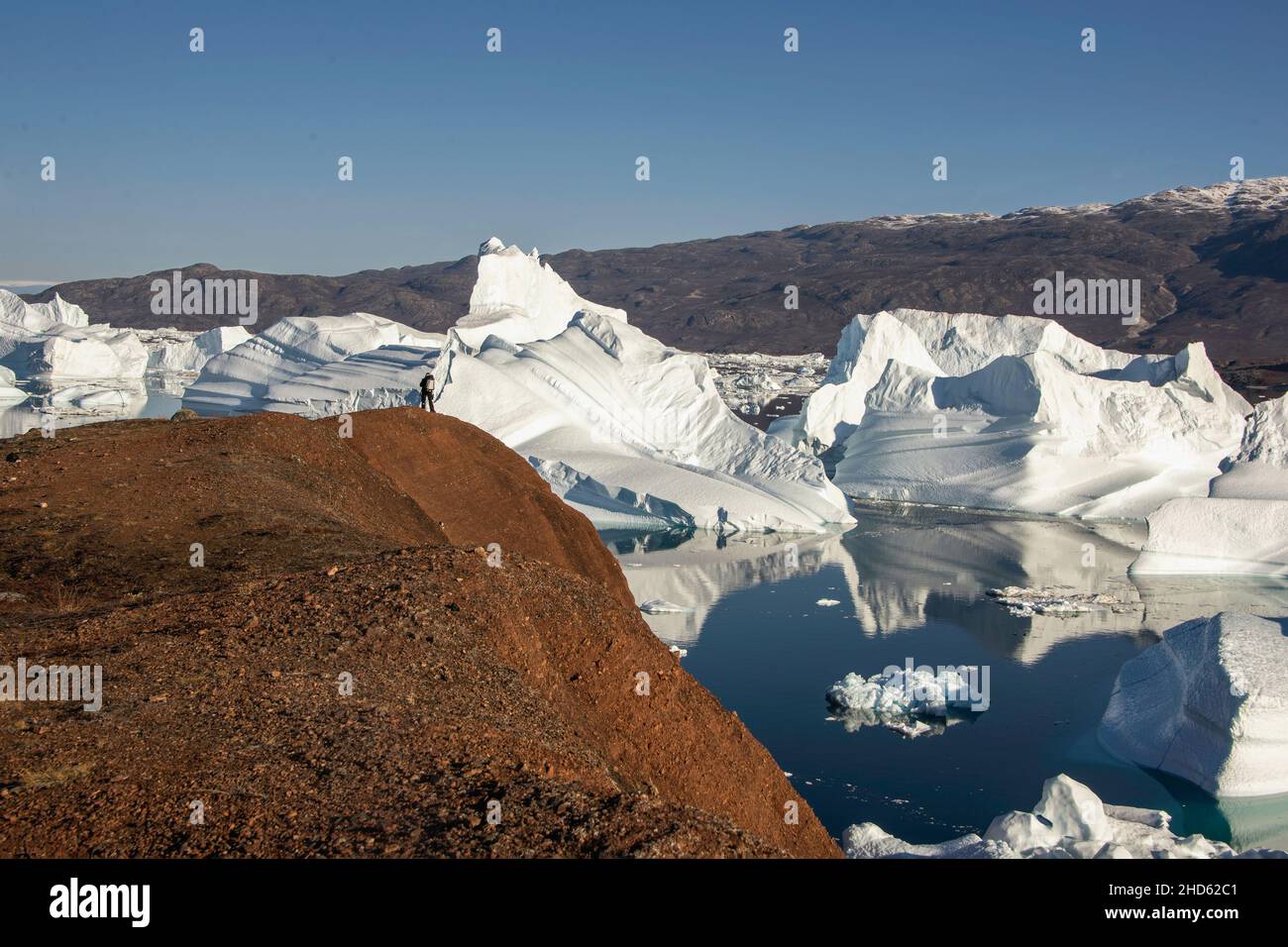 Tiny figure overlooking an ice jam from Rode O, Rodefjord with Milne Land, Scoresby Sund, East Greenland Stock Photo