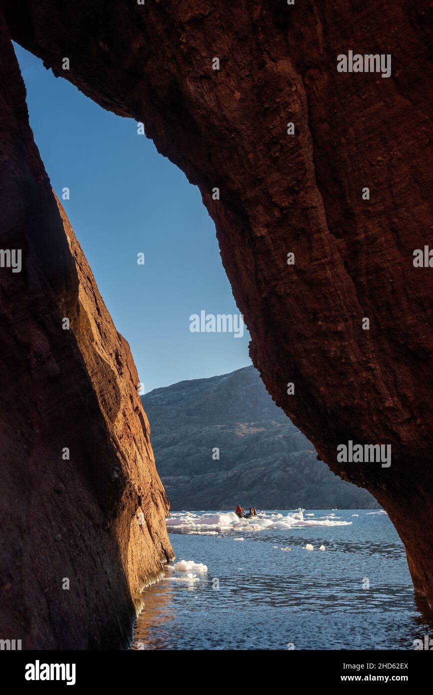 Zodiac off Milne Land seen through a sandstone arch on Rode O, Rodefjord, Scoresby Sund, Greenland Stock Photo