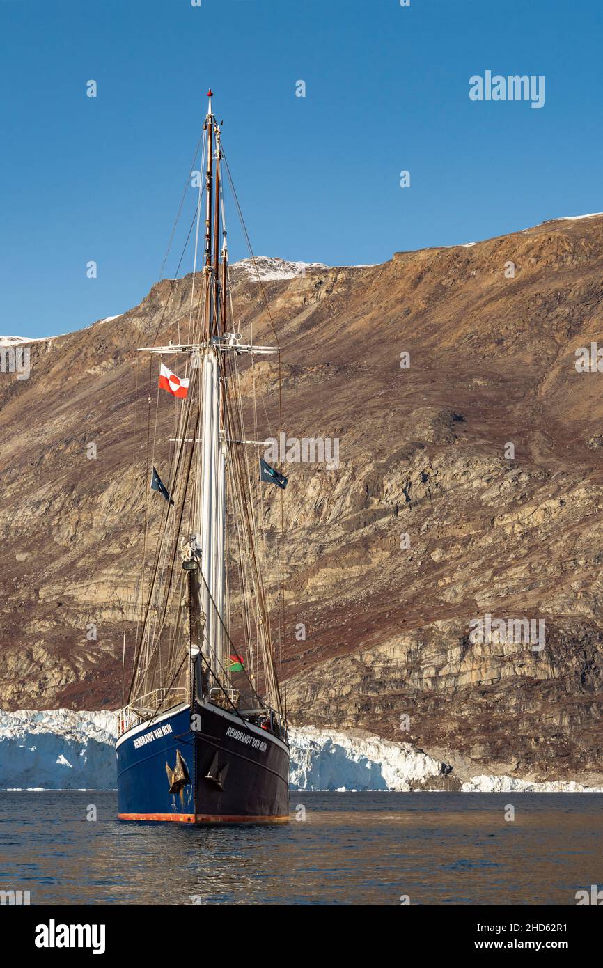 MV Rembrant van Rijn flying the Greenland flag by the toe of the Rolige Brae Glacier, Rodefjord, Scoresby Sund, Greenland Stock Photo