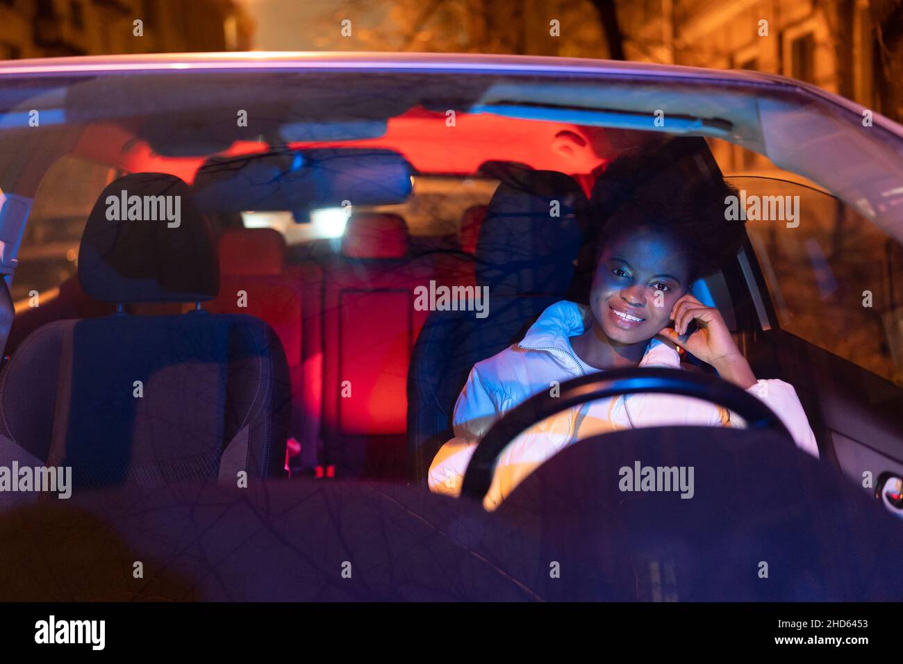 Happy african american woman sits in car behind steering wheel, smiling