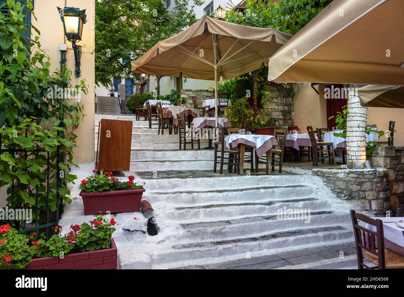 Street restaurant or cafe at Acropolis foot in Plaka district, Athens, Greece. Plaka is tourist attraction of Athens. Cozy narrow alley with stairway Stock Photo