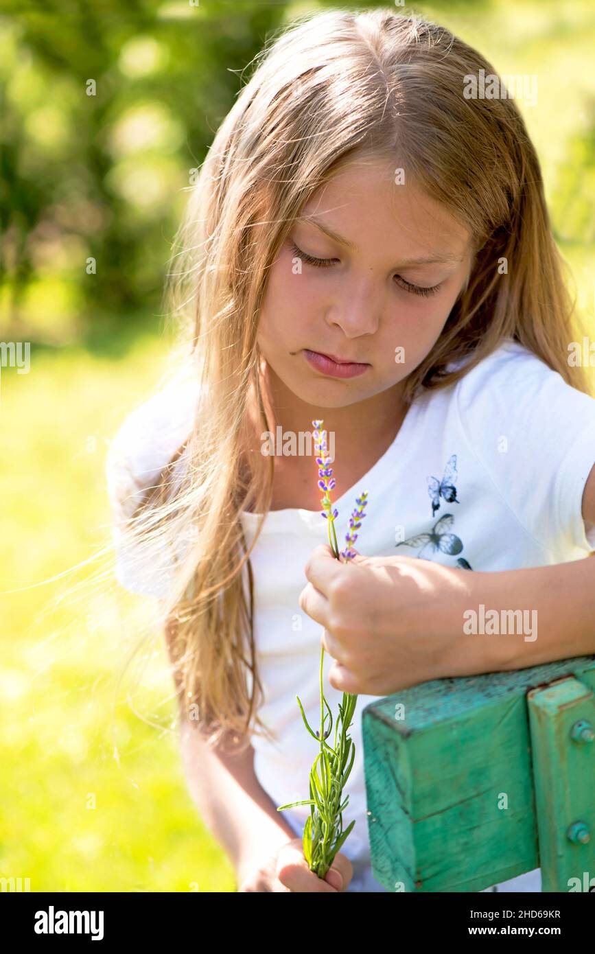 pensive girl sits on a bench with a bouquet of flowers near a private house Stock Photo