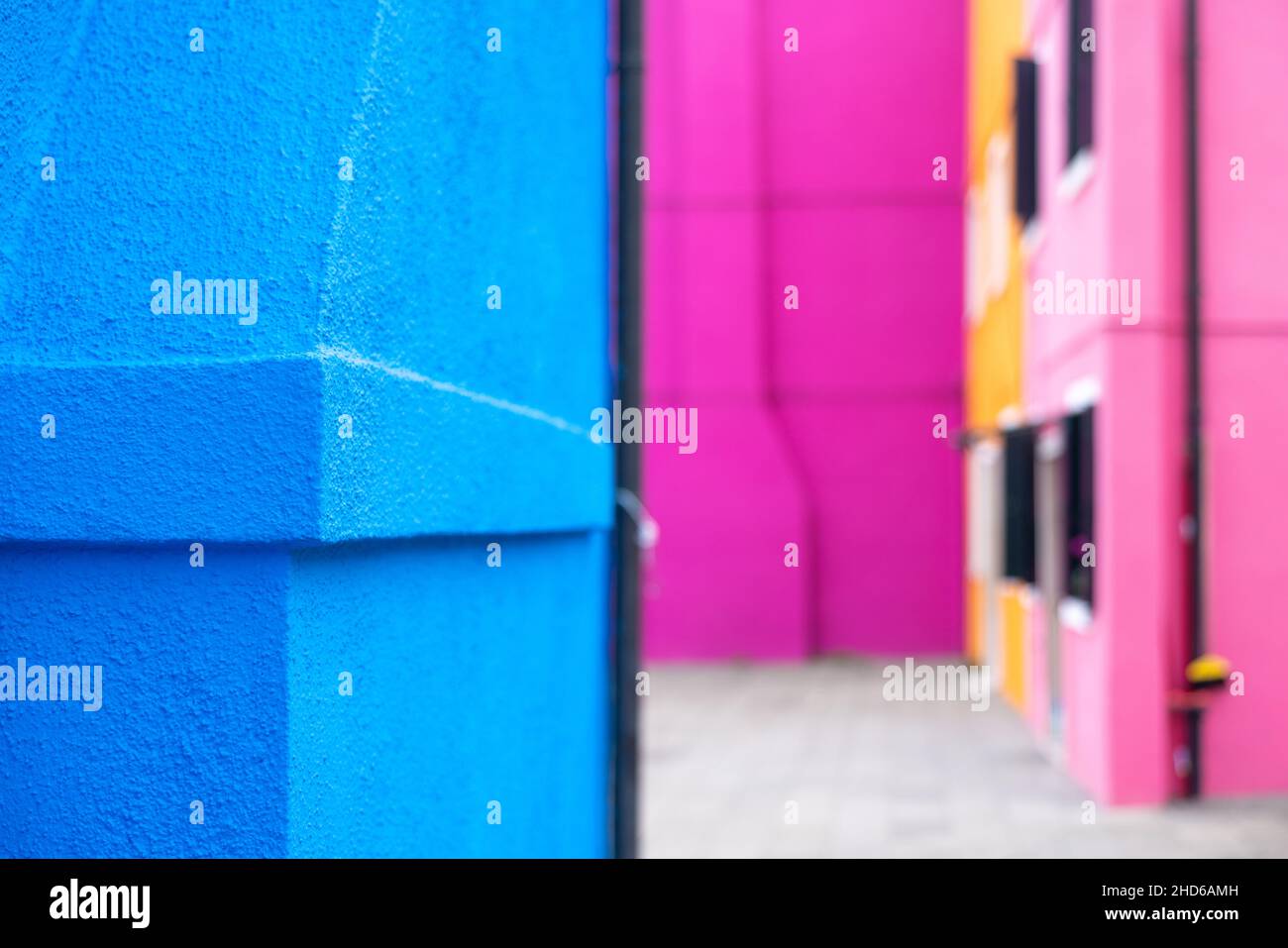 Close up of the corner of a vivid blue plaster facade with a rough surface, against a colorful pink bokeh background Stock Photo