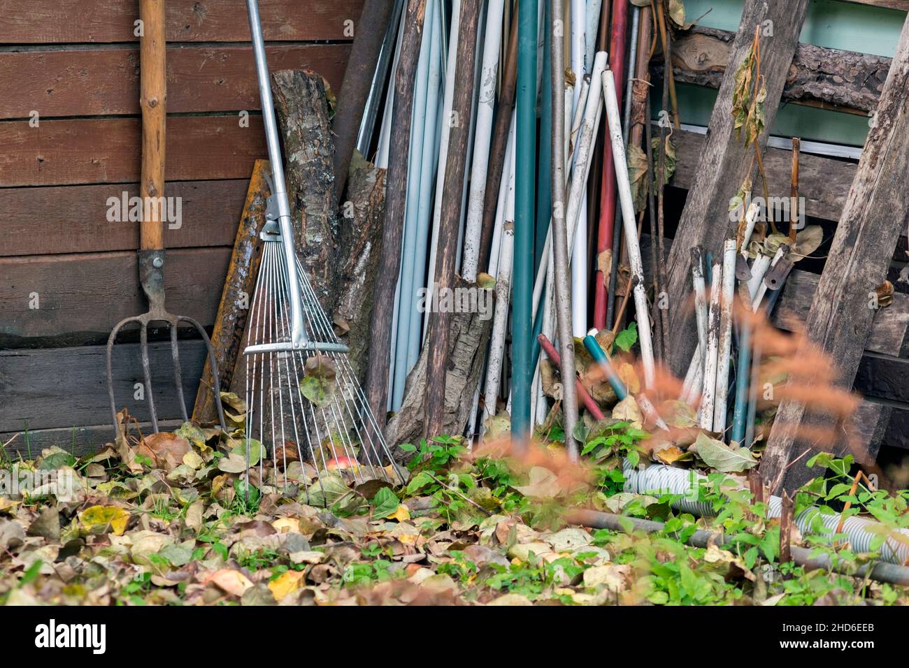 pitchfork, rake and plastic pipes leaning against wooden barn Stock