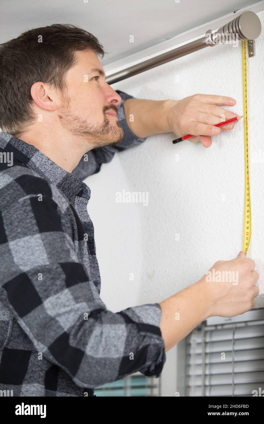man measuring under a curtain rail Stock Photo