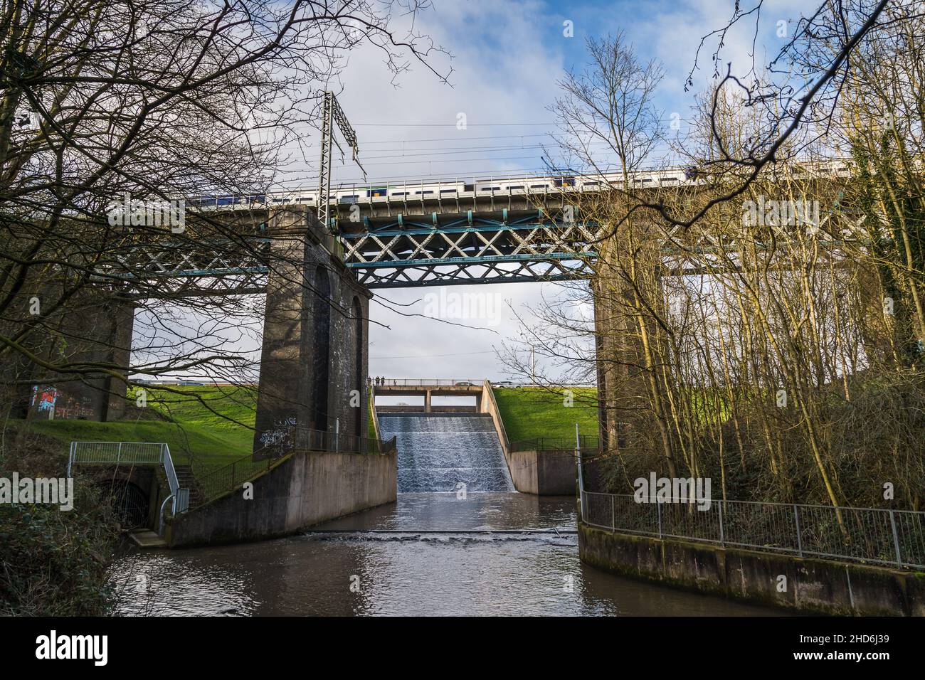 A train passes over a high bridge over the flowing the Carr Mill Dam near St Helens, Merseyside on 3 January 2022. Stock Photo