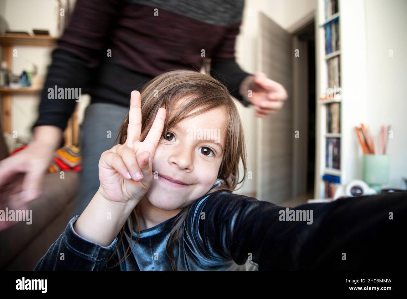 Loving child girl taking selfie by phone with dad indoor in living room, making victory sign Stock Photo