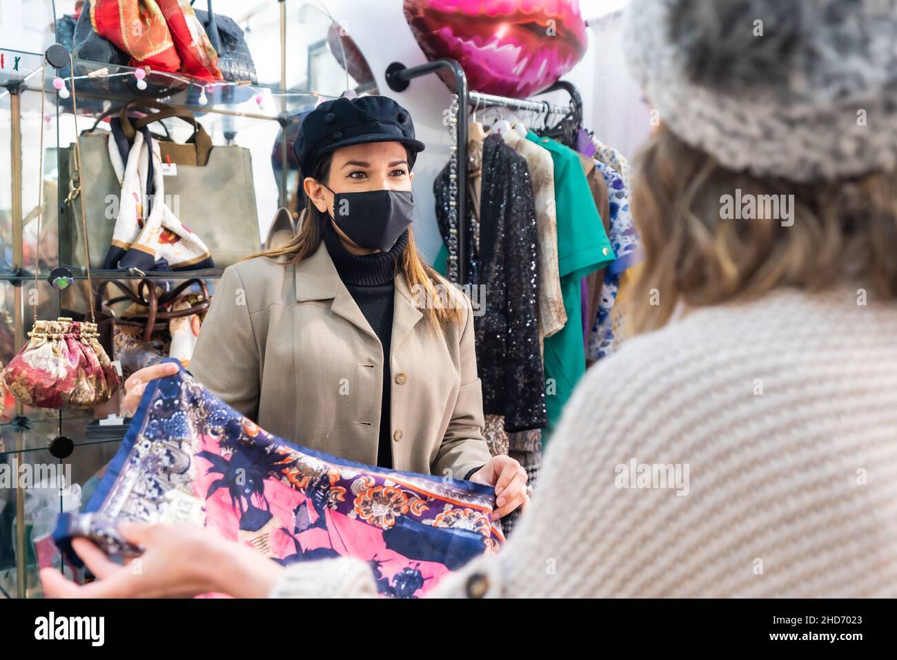Employee of a second-hand clothing store showing clothes to a customer, working with security measures in the coronavirus pandemic Stock Photo